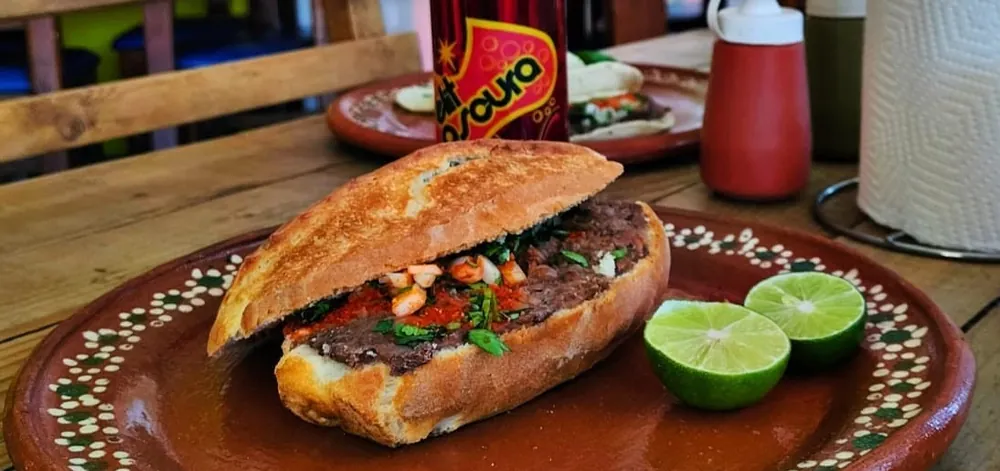 Lonche de barbacoa en bolillo dorado con pico de gallo y limones